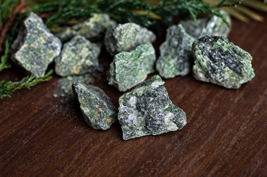 Several rough, green and black speckled stones rest on a dark wooden surface with green foliage in the background.