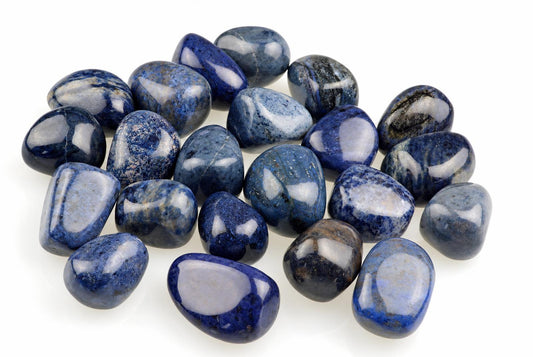 A pile of polished dumortierite stones in dark blue and white on a pale surface.