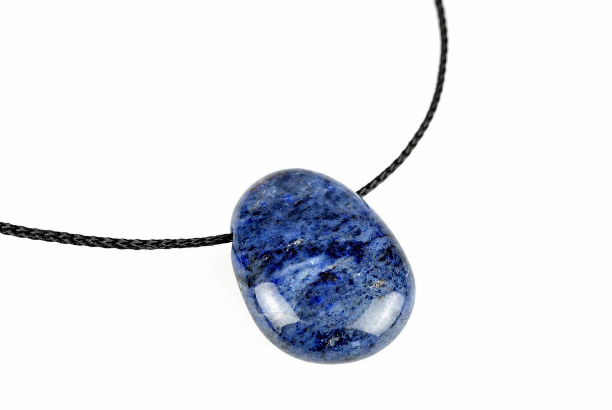 A polished dumortierite pendant with deep blue and white speckles hangs on a black cord against a white background.