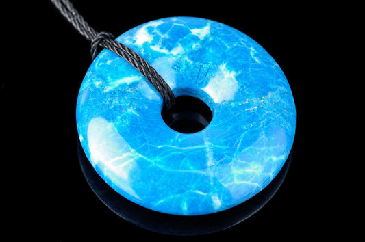 A blue and white patterned donut-shaped pendant with a central hole, threaded on a dark cord against a black background.