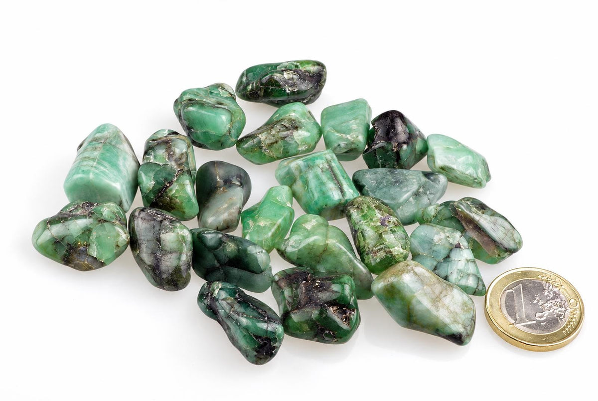 A pile of polished green stones with dark inclusions on a white surface, next to a one euro coin.