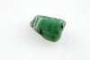 A polished green stone with dark inclusions rests on a pale surface.