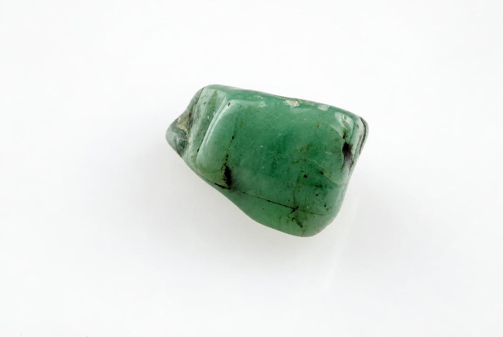 A polished green stone with dark inclusions rests on a pale surface.