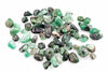A pile of rough, unpolished emerald stones in various shades of green and black on a white surface.