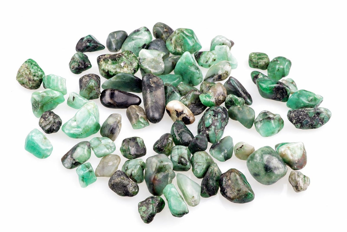 A pile of rough, unpolished emerald stones in various shades of green and black on a white surface.