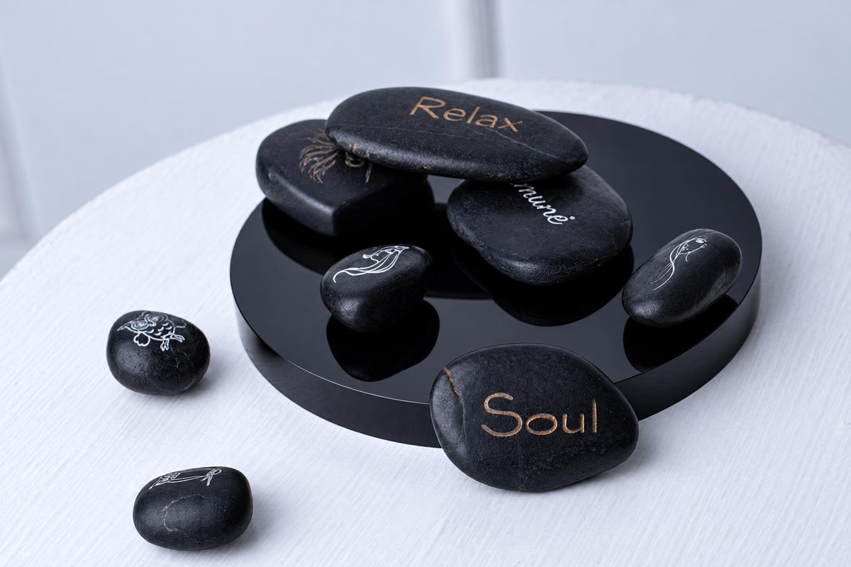 Smooth black stones engraved with words and line drawings are arranged on and around a round black tray on a pale surface.