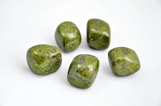 Five polished, rounded stones with green and dark speckled patterns on a white surface.