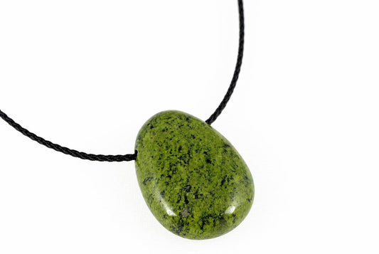 A polished green pendant with black speckles hangs from a dark cord against a white background.