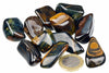 A pile of polished, dark stones with golden and white banding on a white surface, next to a one-euro coin.