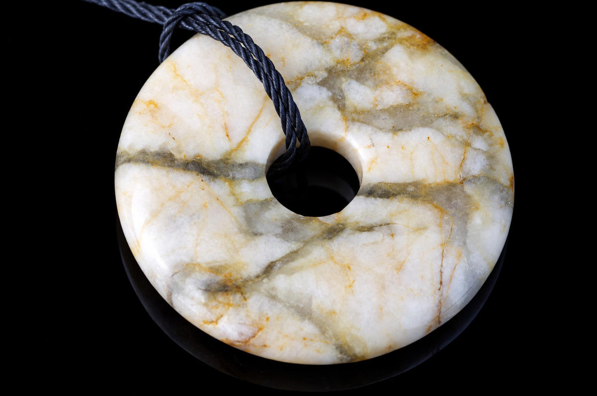 A round, donut-shaped pendant with a central hole, featuring white and grey veining on a dark surface.