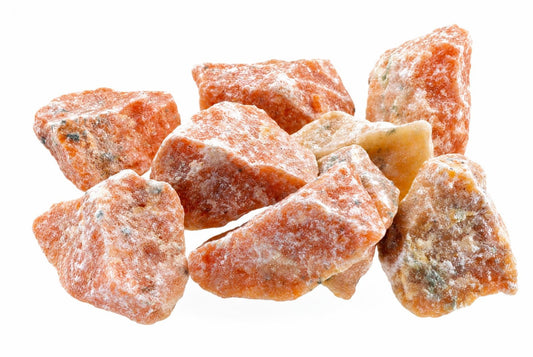 A pile of raw fire calcite crystals, orange with white and dark flecks, on a pale surface.