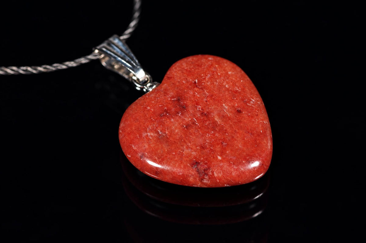 A polished red heart-shaped pendant with a silver-toned bail and twisted chain, resting on a dark reflective surface.