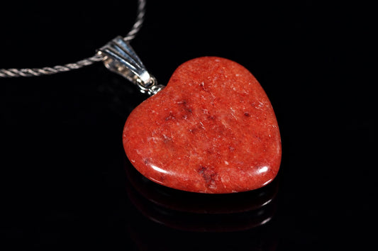 A polished red heart-shaped pendant with a silver-toned bail and twisted chain, resting on a dark reflective surface.