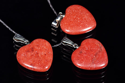 Polished red heart-shaped pendants on black cords lie on a dark reflective surface.