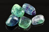 Five polished fluorite stones in green, blue and purple hues rest on a dark reflective surface.