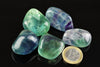 Five polished fluorite stones in green, blue and purple hues rest on a dark surface next to a one euro coin.
