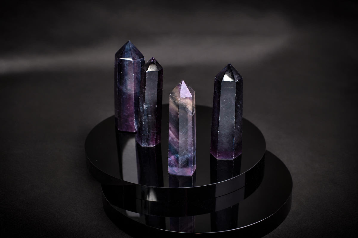 Four polished fluorite crystals with purple and grey hues stand on a dark, reflective circular base.