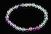 A bracelet of round beads in pale green, clear and purple tones on a dark surface.