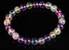 A bracelet of round beads in purple, blue, green and pale tones on a dark surface.