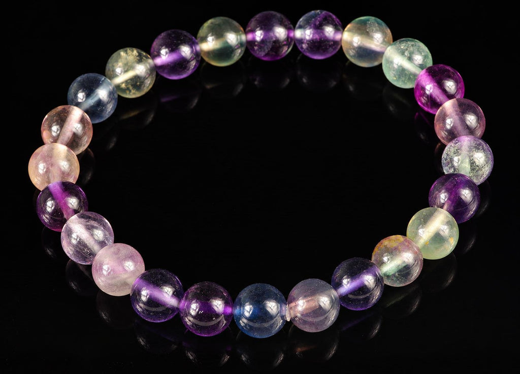 A bracelet of round beads in purple, blue, green and pale tones on a dark surface.