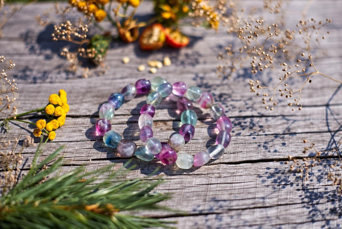 A bracelet with smooth, oval beads in purple, blue, green and clear fluorite colours lies on a weathered wooden surface.
