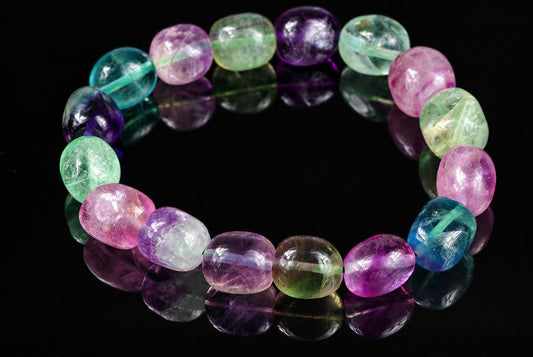 A bracelet of polished fluorite beads in purple, green, blue and pink on a dark reflective surface.