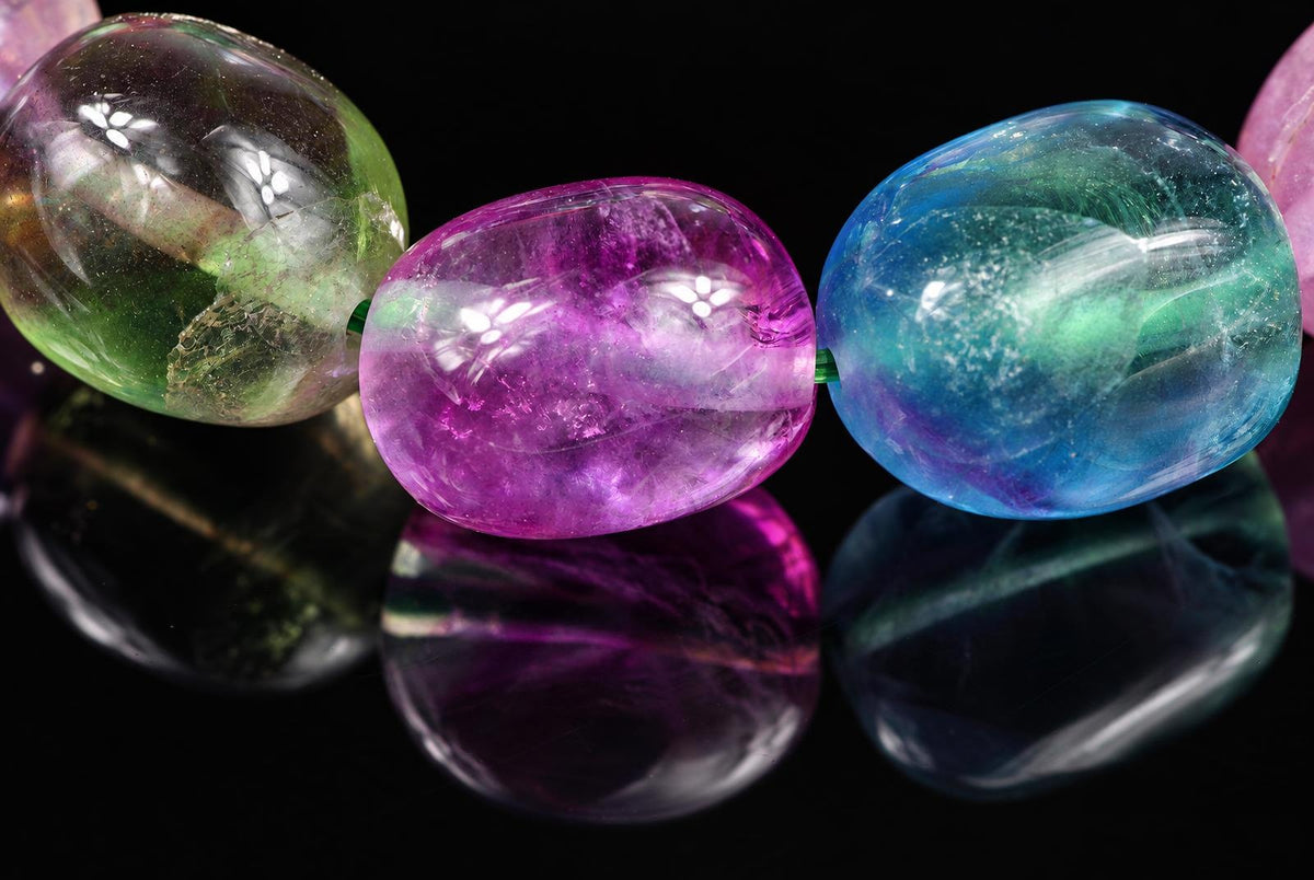 Three polished fluorite beads in green, purple and blue colours on a dark reflective surface.