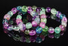 A bracelet of oval fluorite beads in purple, green, blue and pink on a dark surface.