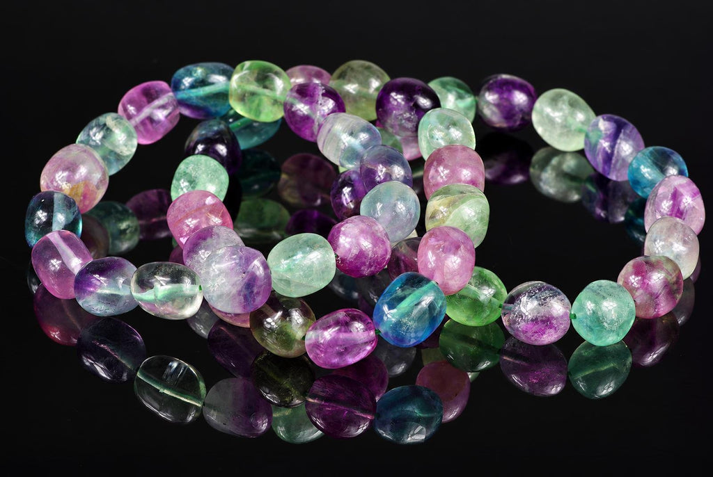 A bracelet of oval fluorite beads in purple, green, blue and pink on a dark surface.