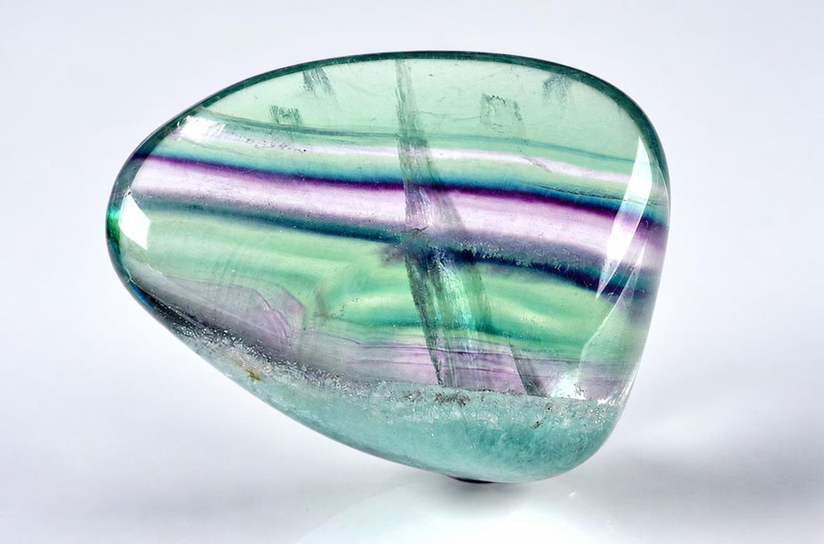 A polished fluorite crystal with green, purple and blue bands on a pale surface.
