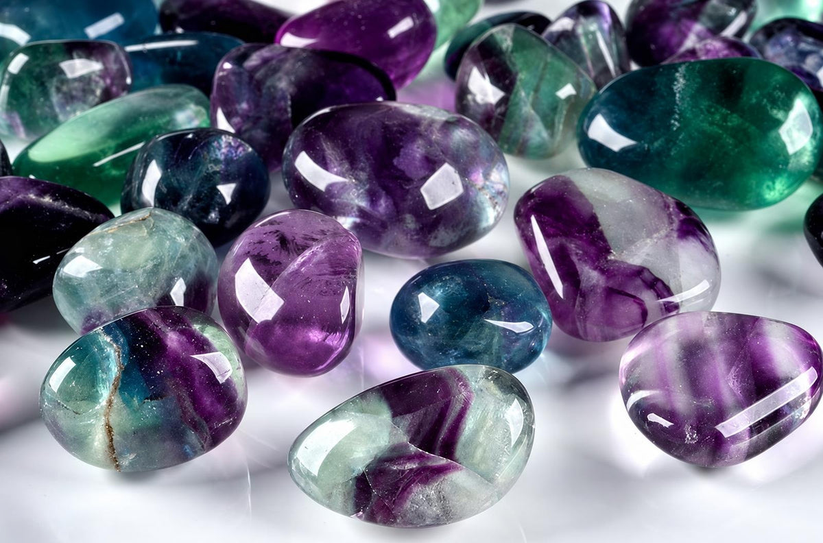 A collection of polished fluorite stones in purple, green, blue and white on a pale surface.