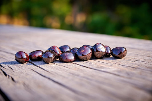 A group of polished, dark red to brownish stones with a glossy finish rests on a weathered wooden surface.