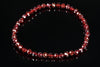 A bracelet of faceted red beads on a dark reflective surface.