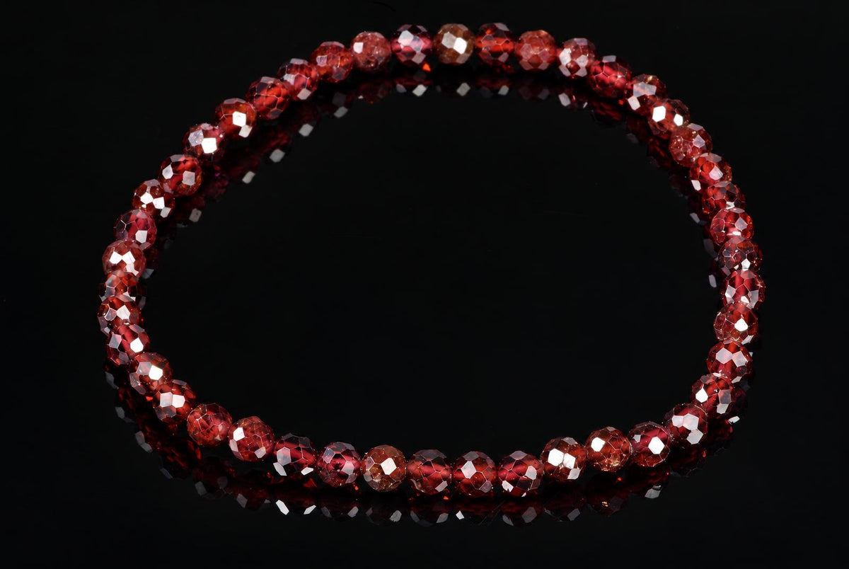 A bracelet of faceted red beads on a dark reflective surface.