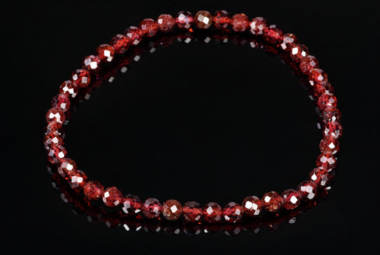 A bracelet of faceted red beads on a dark reflective surface.