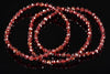 A faceted red garnet bracelet with multiple strands of round beads arranged in a coil on a dark reflective surface.
