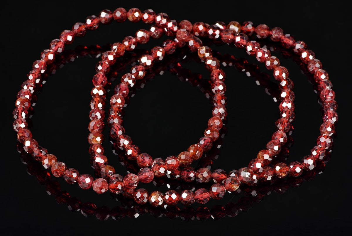 A faceted red garnet bracelet with multiple strands of round beads arranged in a coil on a dark reflective surface.