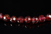 A row of faceted red garnet beads on a dark reflective surface.