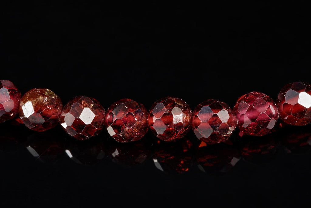 A row of faceted red garnet beads on a dark reflective surface.