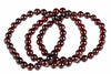 A strand of round, dark red garnet beads arranged in a loose coil on a white surface.
