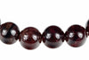 A row of round, polished beads in dark red and black with silver-toned reflections on a white surface.