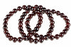 A strand of round, dark red beads with a glossy finish arranged in loops on a white background.