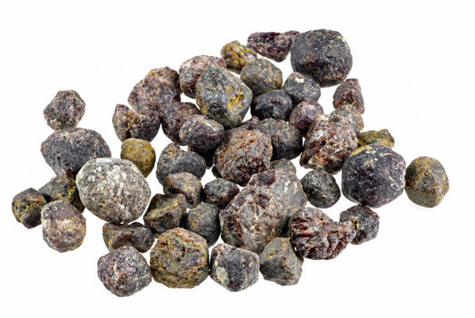 A pile of raw garnet stones in dark red, brown and yellow tones on a white background.