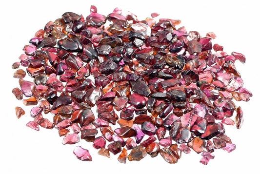 A pile of small, rough-cut garnet stones in shades of pink, red, and dark brown on a white background.