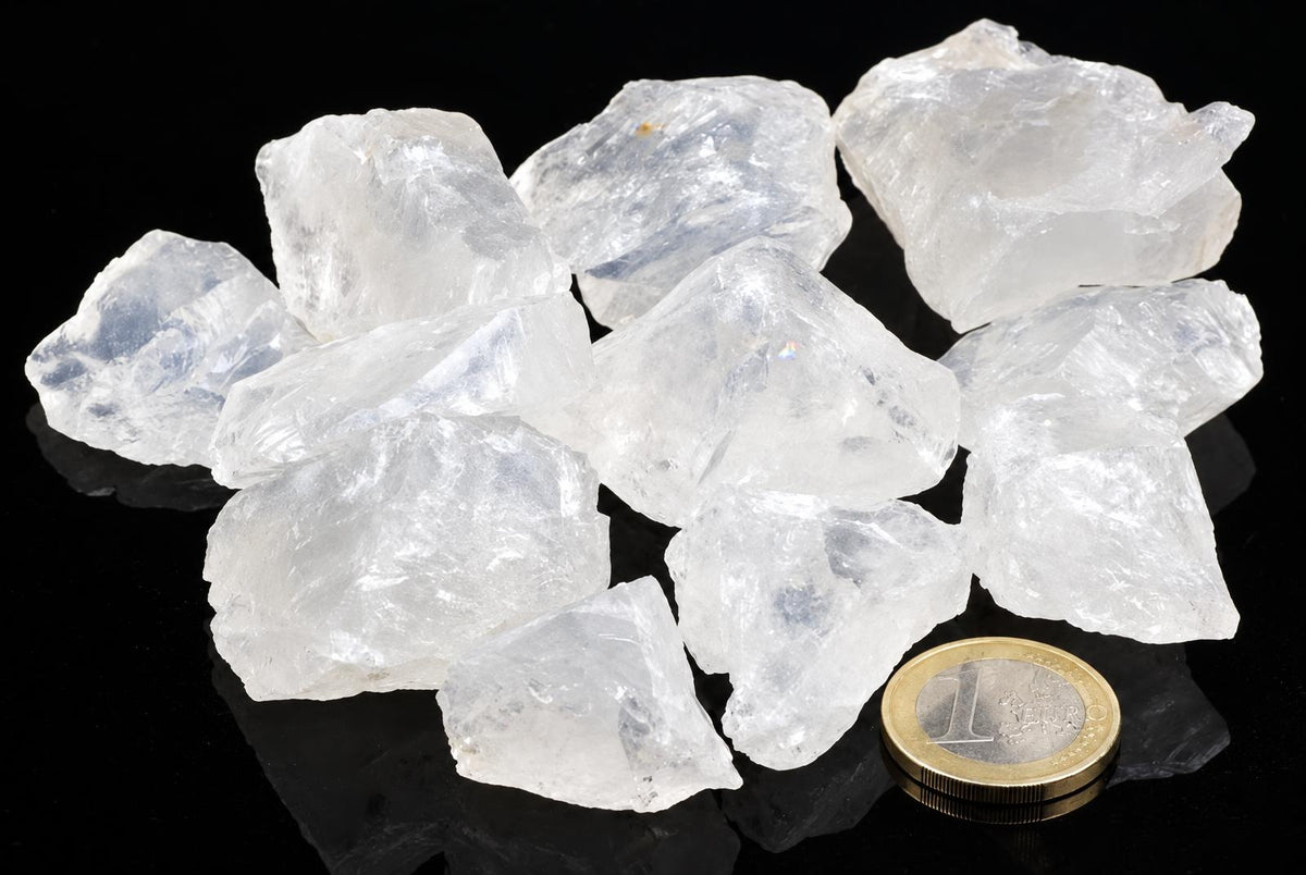 A pile of clear, translucent white crystals on a dark surface with a one-euro coin for scale.