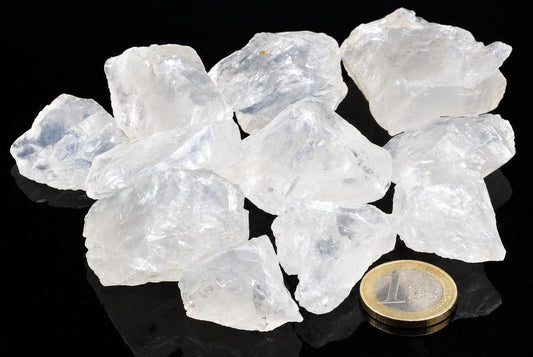 A pile of clear, translucent white crystals on a dark surface with a one-euro coin for scale.