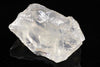 A large, clear, translucent crystal with a rough, angular shape rests on a dark surface against a black background.