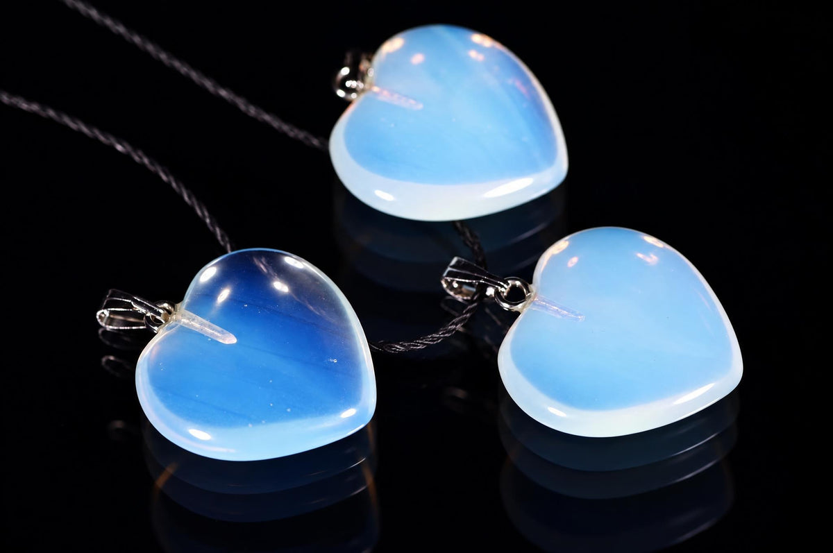 Translucent blue heart-shaped pendants on black cords rest on a dark reflective surface.
