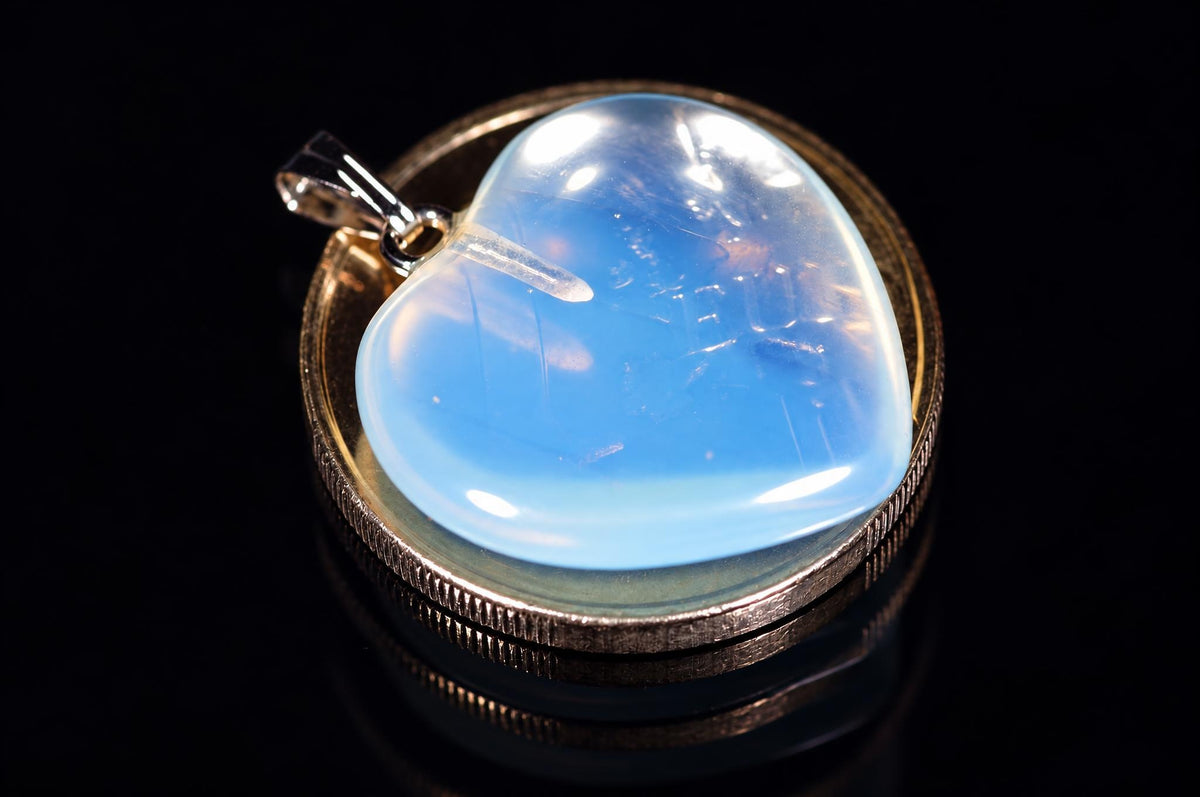 A heart-shaped glass opal pendant with a silver-toned bail, set in a gold-coloured bezel on a dark reflective surface.