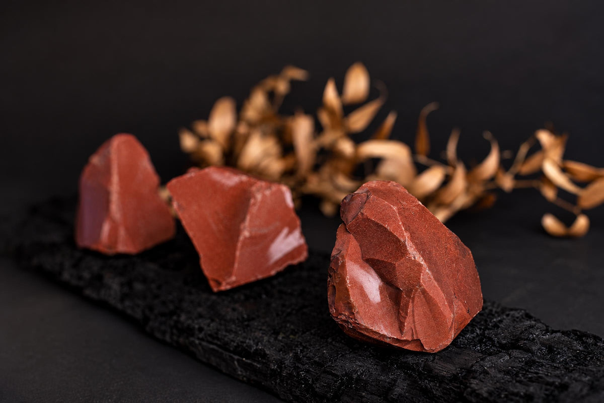 Three red, rough-textured stones on a dark surface with dried plant stems in the background.